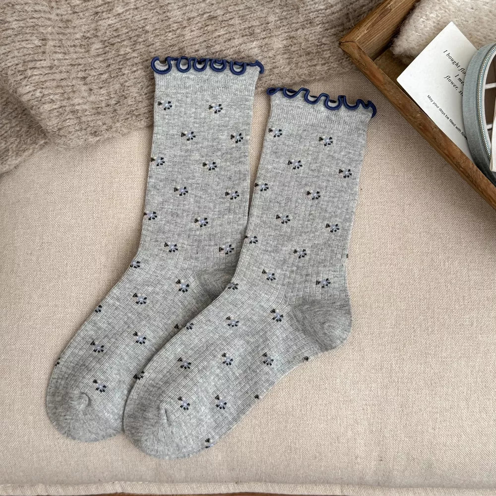 Pair of gray socks with small dark motifs and navy scalloped cuffs laid flat