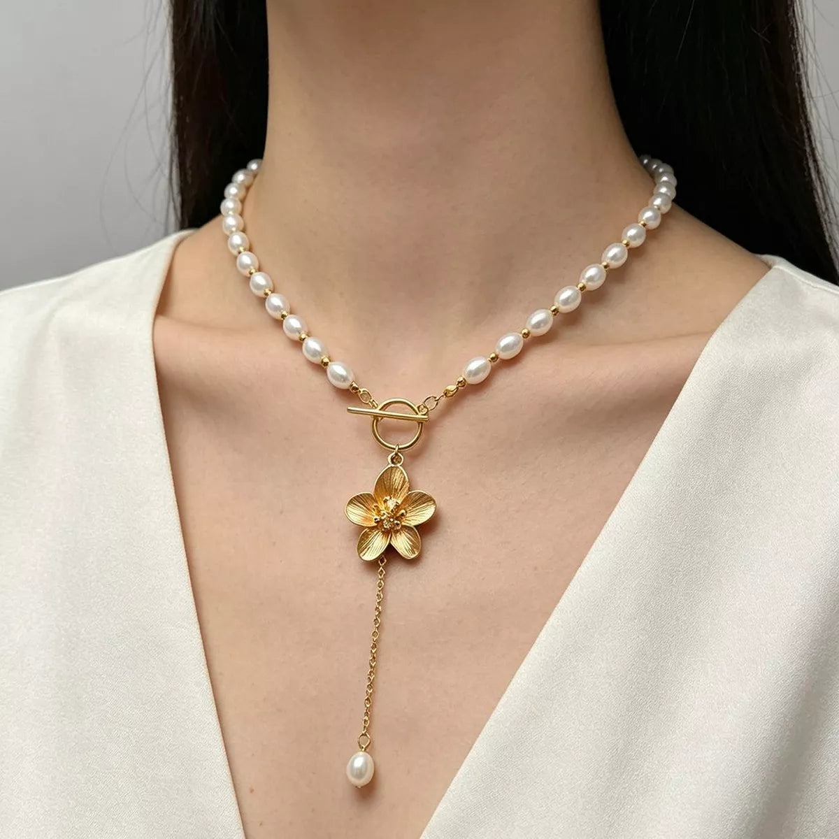 Gold flower pendant and pearl drop on a pearl choker, shown over a white blouse