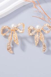 Pair of gold-tone bow earrings with white bead tops on a pale surface