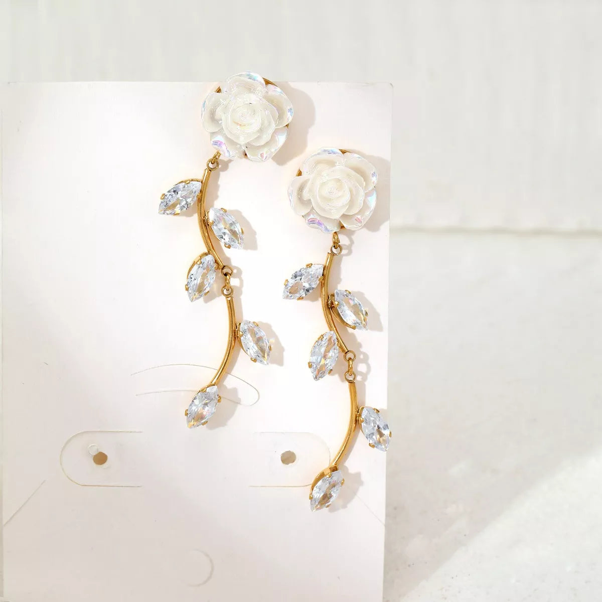Pair of gold-tone flower drop earrings with curved stems and clear accents on display card