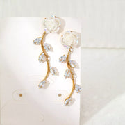 Pair of gold-tone flower drop earrings with curved stems and clear accents on display card