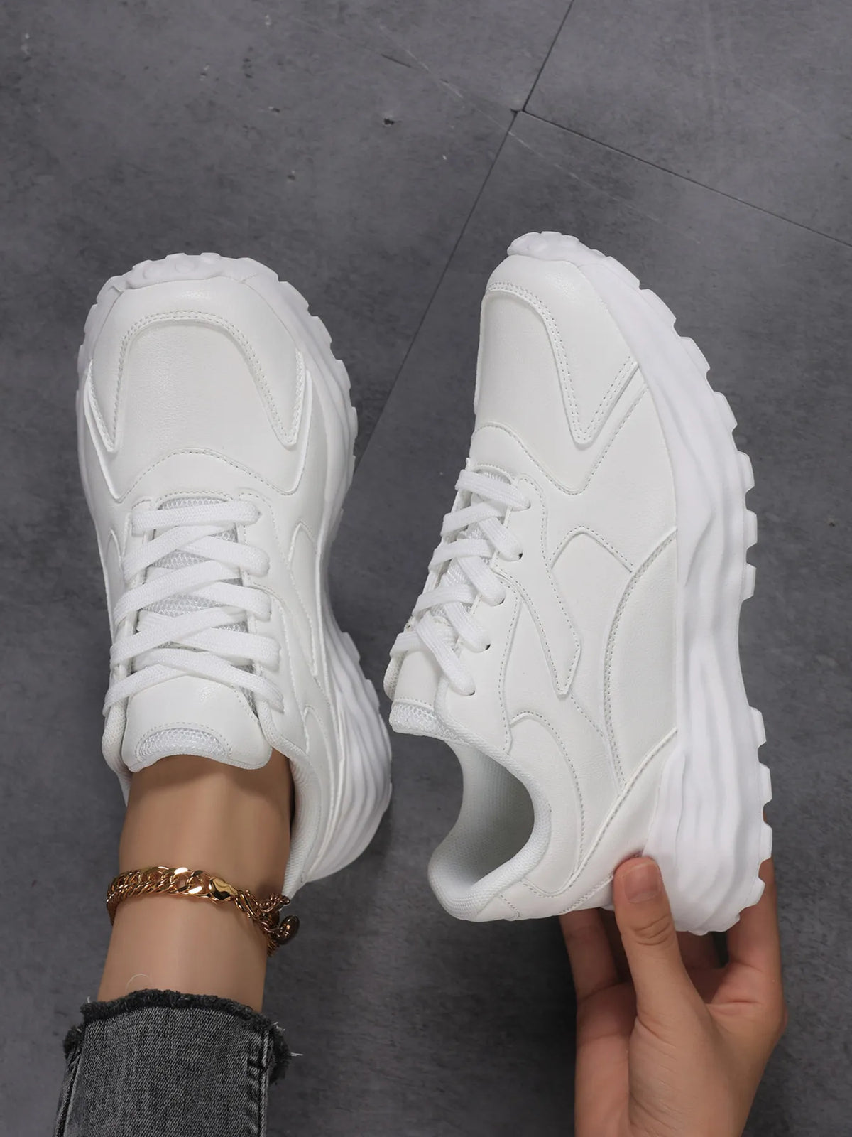 White chunky trainers with one shoe worn and the other held to show its side panel