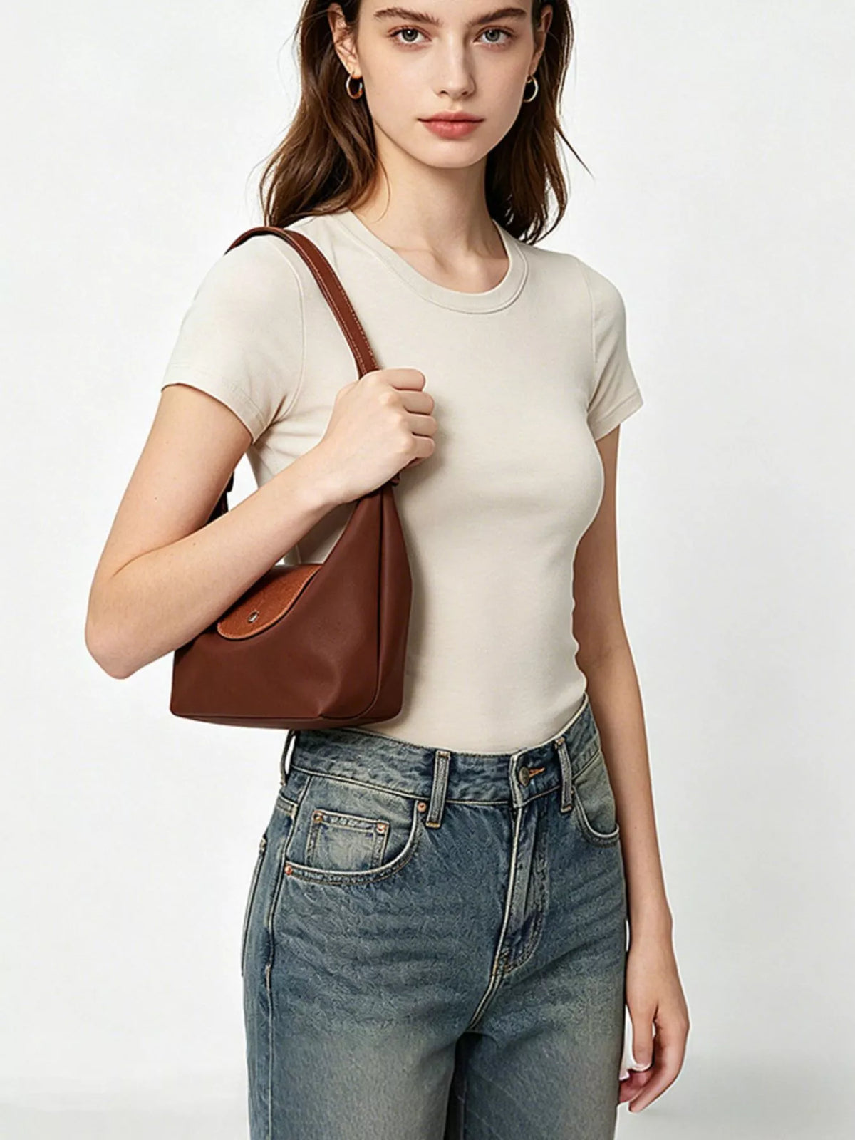Model wearing the brown shoulder bag tucked under the arm, with the front flap visible.