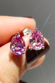 Pink teardrop stud earrings held between fingers against a dark background