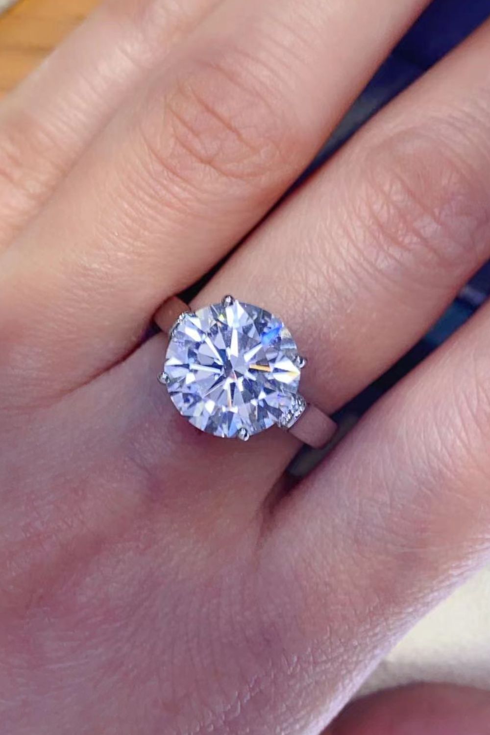 Round moissanite solitaire worn on a finger, showing the bright center stone.