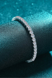 Slim silver moissanite tennis bracelet displayed on a teal velvet stand.
