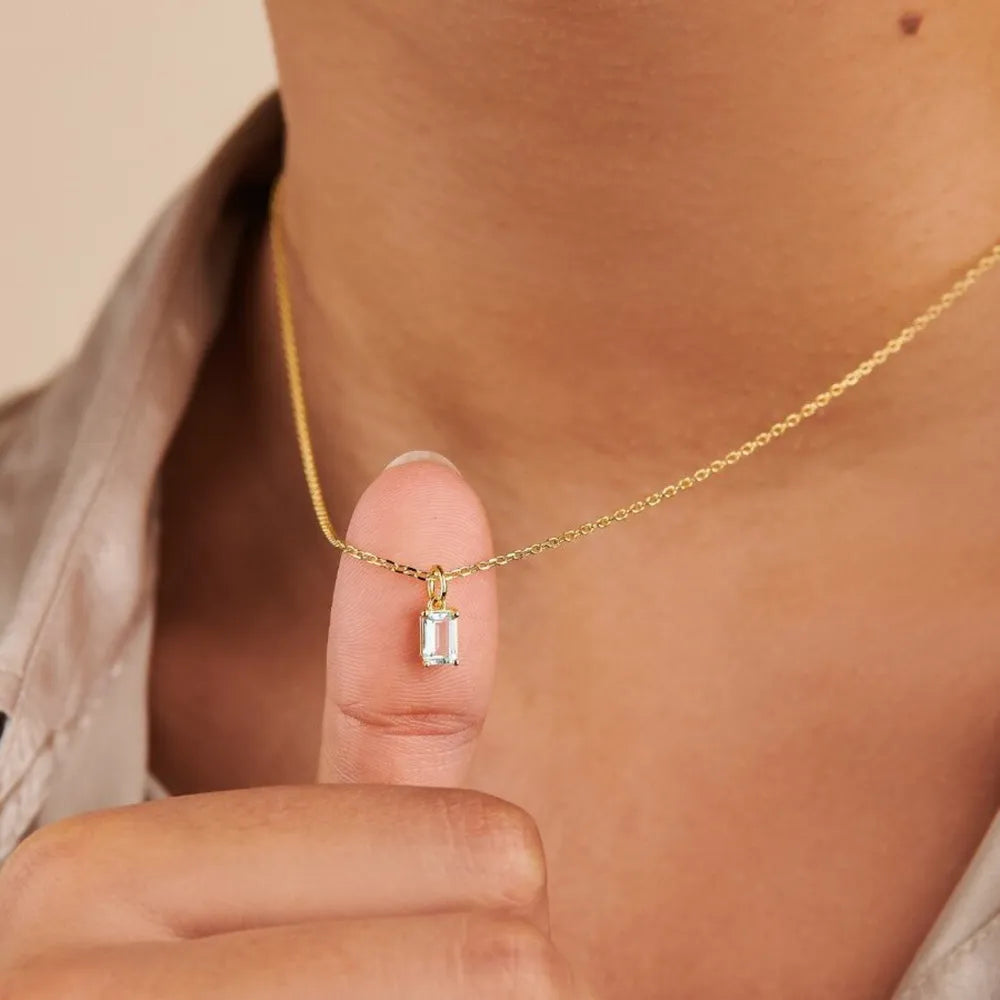 Model holding a clear rectangular pendant on a gold-tone necklace