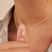 Model holding a clear rectangular pendant on a gold-tone necklace