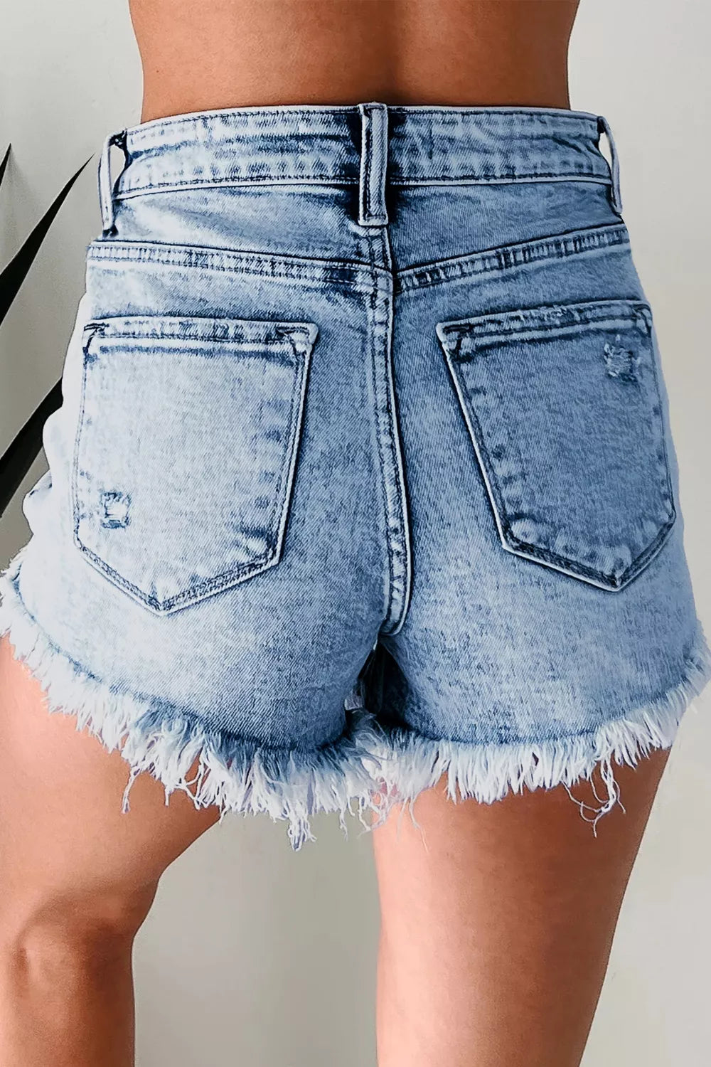 Back view of light-wash denim shorts with two pockets and frayed hems