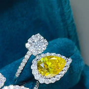 Bypass ring with pear-shaped yellow stone and clear setting styled on dark teal fabric