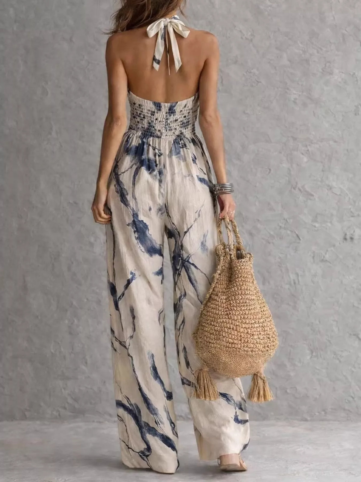 Back of the cream and blue jumpsuit showing its neck bow and smocked upper back.