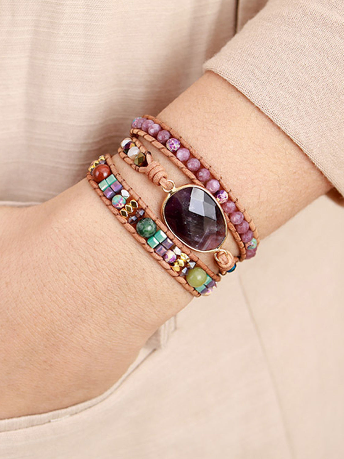 Purple oval stone centerpiece on a triple-layer beaded bracelet worn on a wrist.