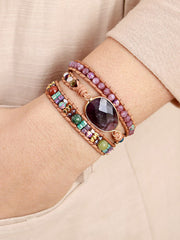 Purple oval stone centerpiece on a triple-layer beaded bracelet worn on a wrist.