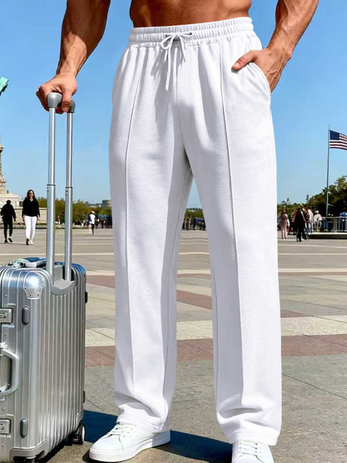 Front view of white wide-leg drawstring pants beside a silver suitcase in a Paris plaza.