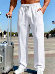 Front view of white wide-leg drawstring pants beside a silver suitcase in a Paris plaza.