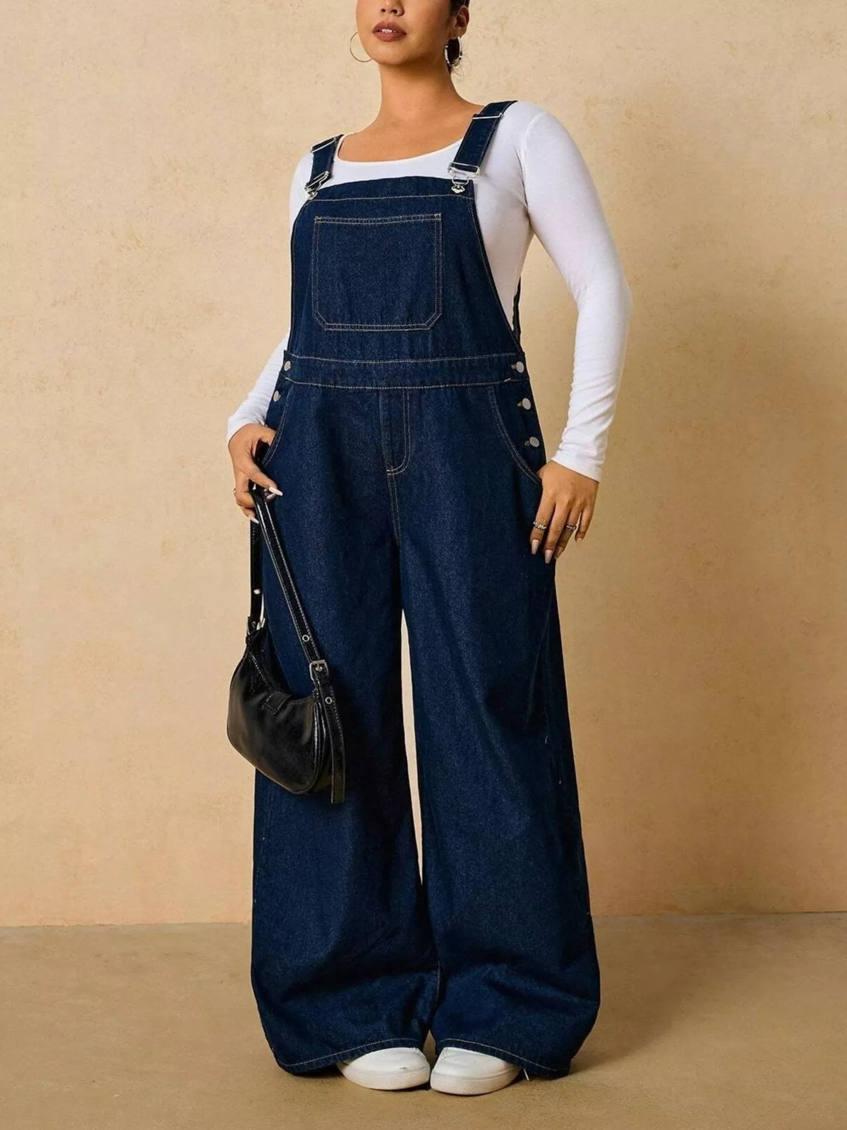 Dark blue denim overalls shown at an angle while holding a small black bag.
