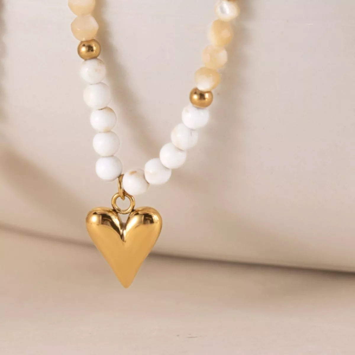 Close-up of gold-tone heart pendant on white and beige beads