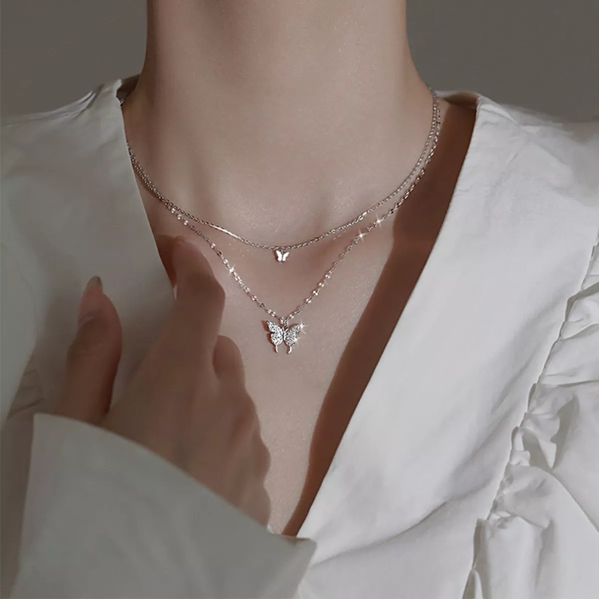 Double-layer silver-tone butterfly necklace worn over a white blouse