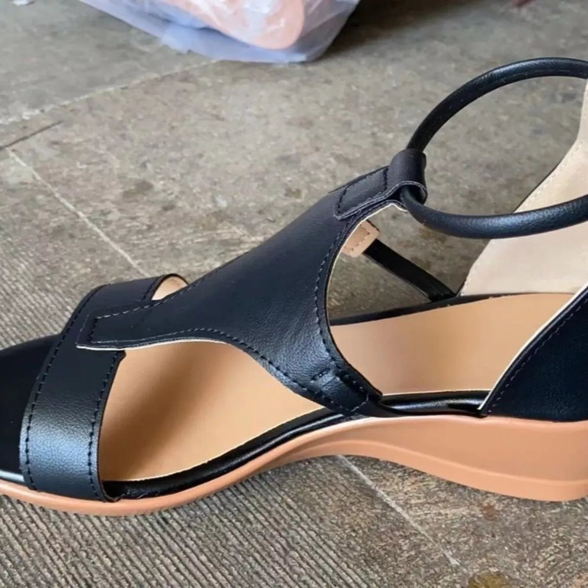 Close side view of black wedge sandal with ankle strap and tan sole