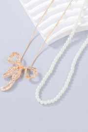 Gold-tone bow pendant on a white beaded necklace beside its gold-tone chain