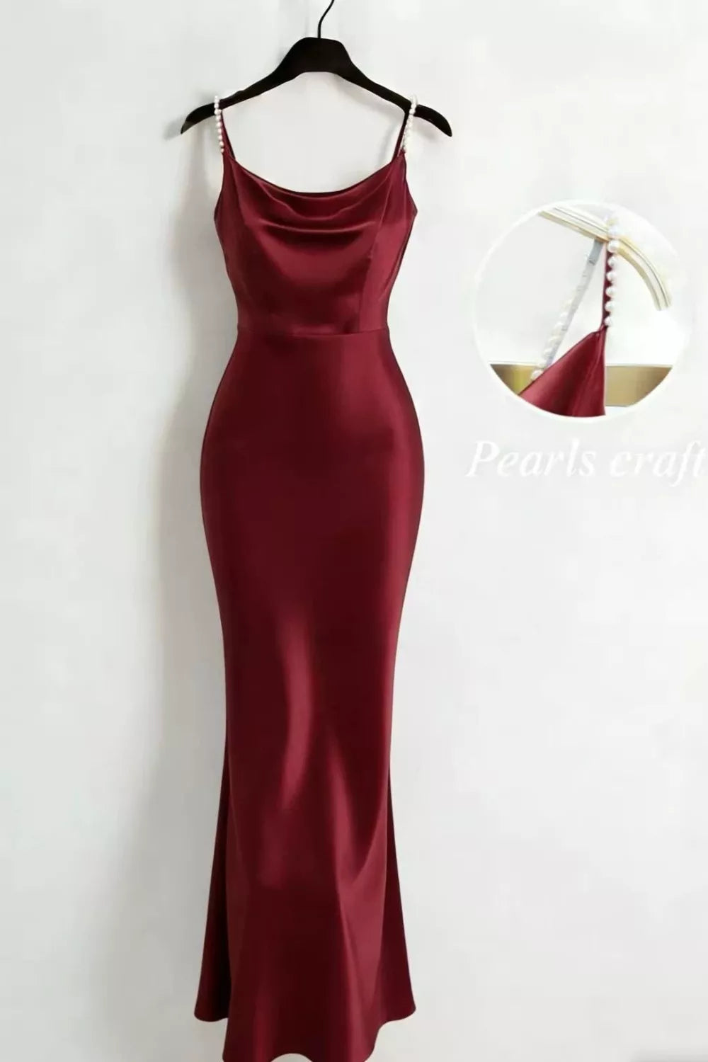 Burgundy satin maxi dress with pearl straps and draped neckline displayed on a hanger.