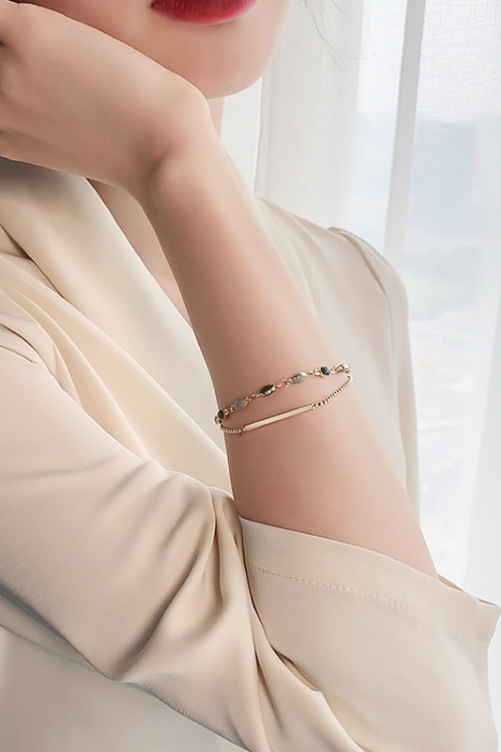Model wearing a layered gold-tone bracelet with green and pale blue stones
