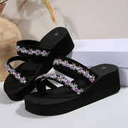 Pair of black platform sandals with purple floral-trim straps displayed on white blocks