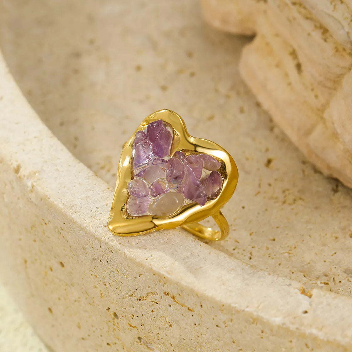 Gold-plated heart-shaped ring with pink stones resting on a pale stone surface