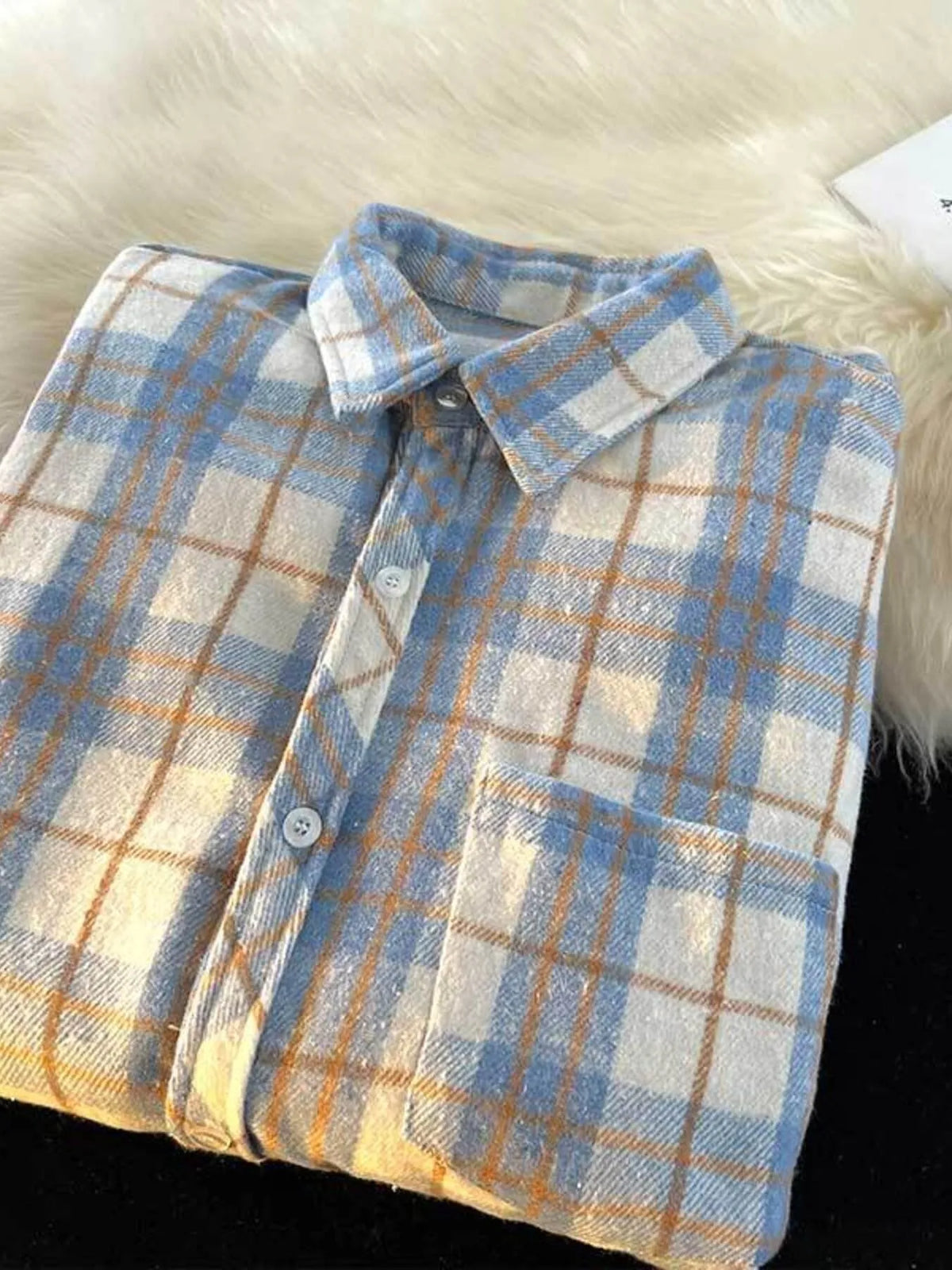 Close view of the blue and cream plaid shirt collar, buttons and single chest pocket