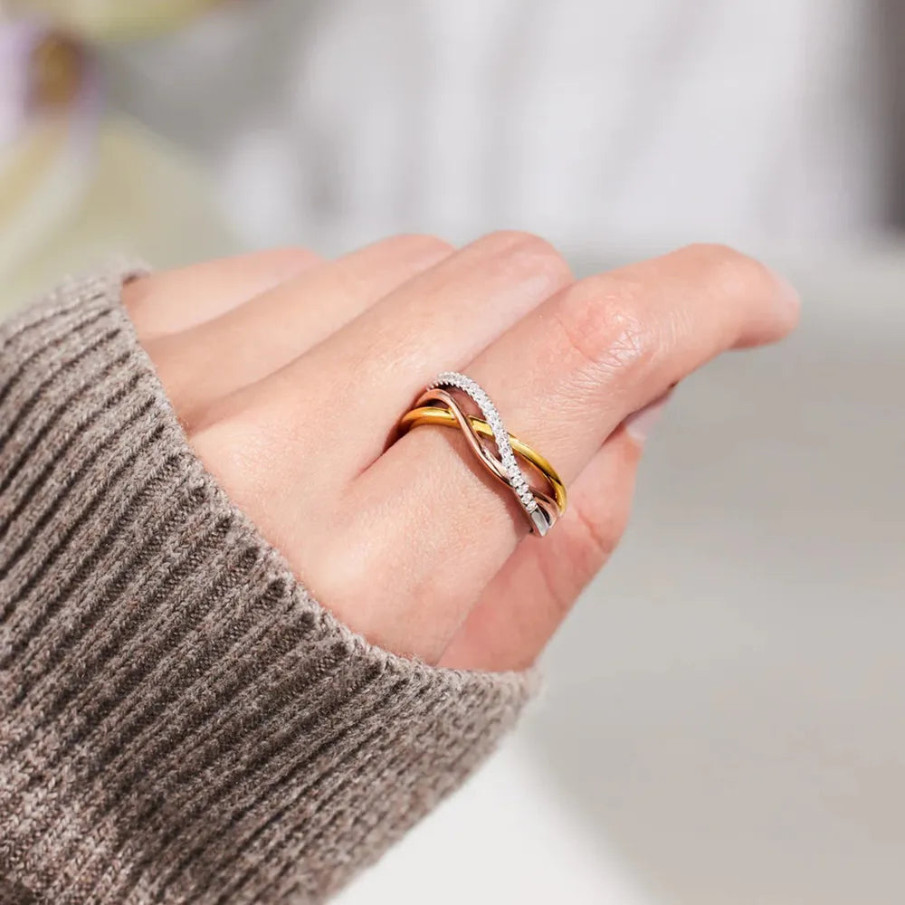 Crisscross two-tone ring worn on a hand in a taupe knit sleeve