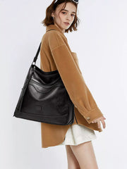 Black multi-pocket handbag worn over a shoulder, showing the curved front pocket and long strap