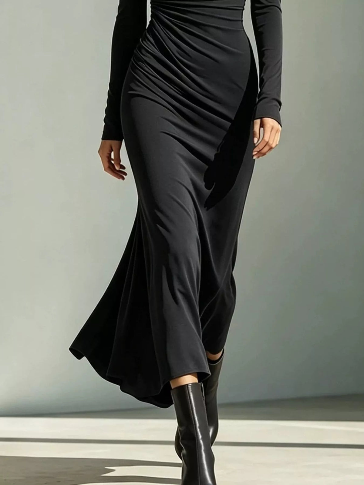 Lower view of the black ruched dress showing its flared hem and black boots.