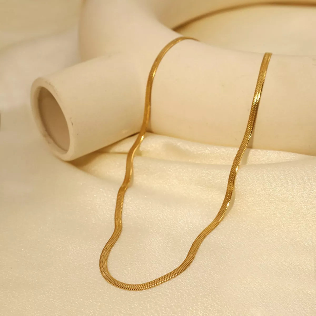 Fine gold-tone chain necklace arranged in a loose curve on cream fabric