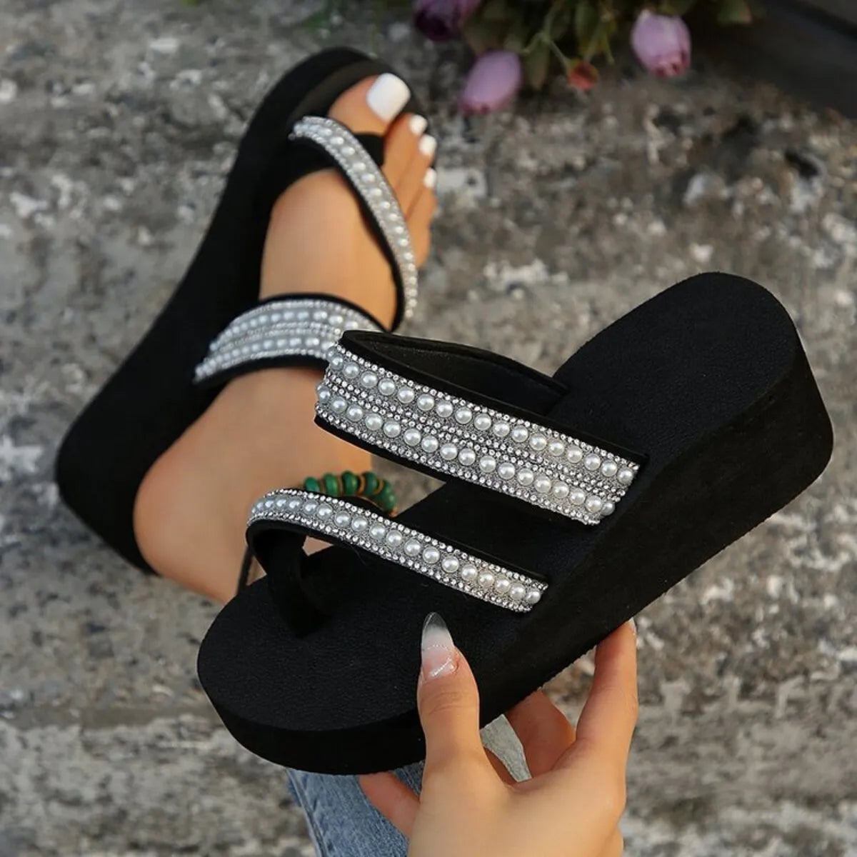 Black embellished wedge sandal held to show its two decorated straps and thick sole