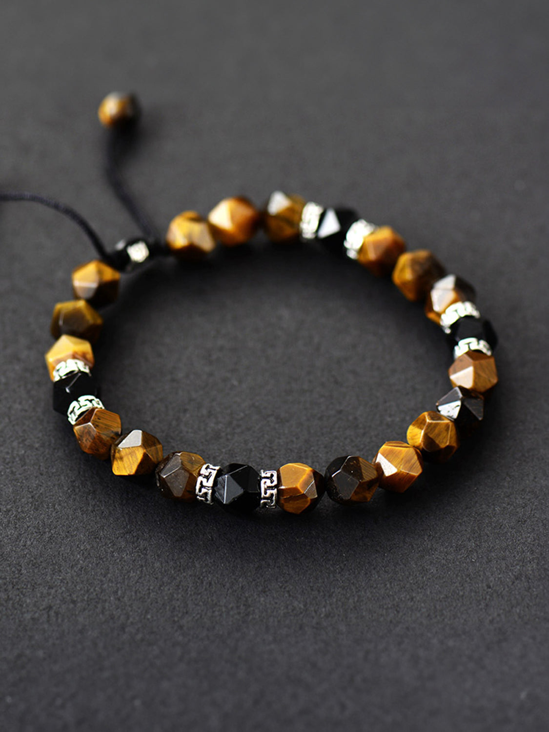 Brown faceted stone bracelet with black and silver-patterned spacer beads on a dark surface