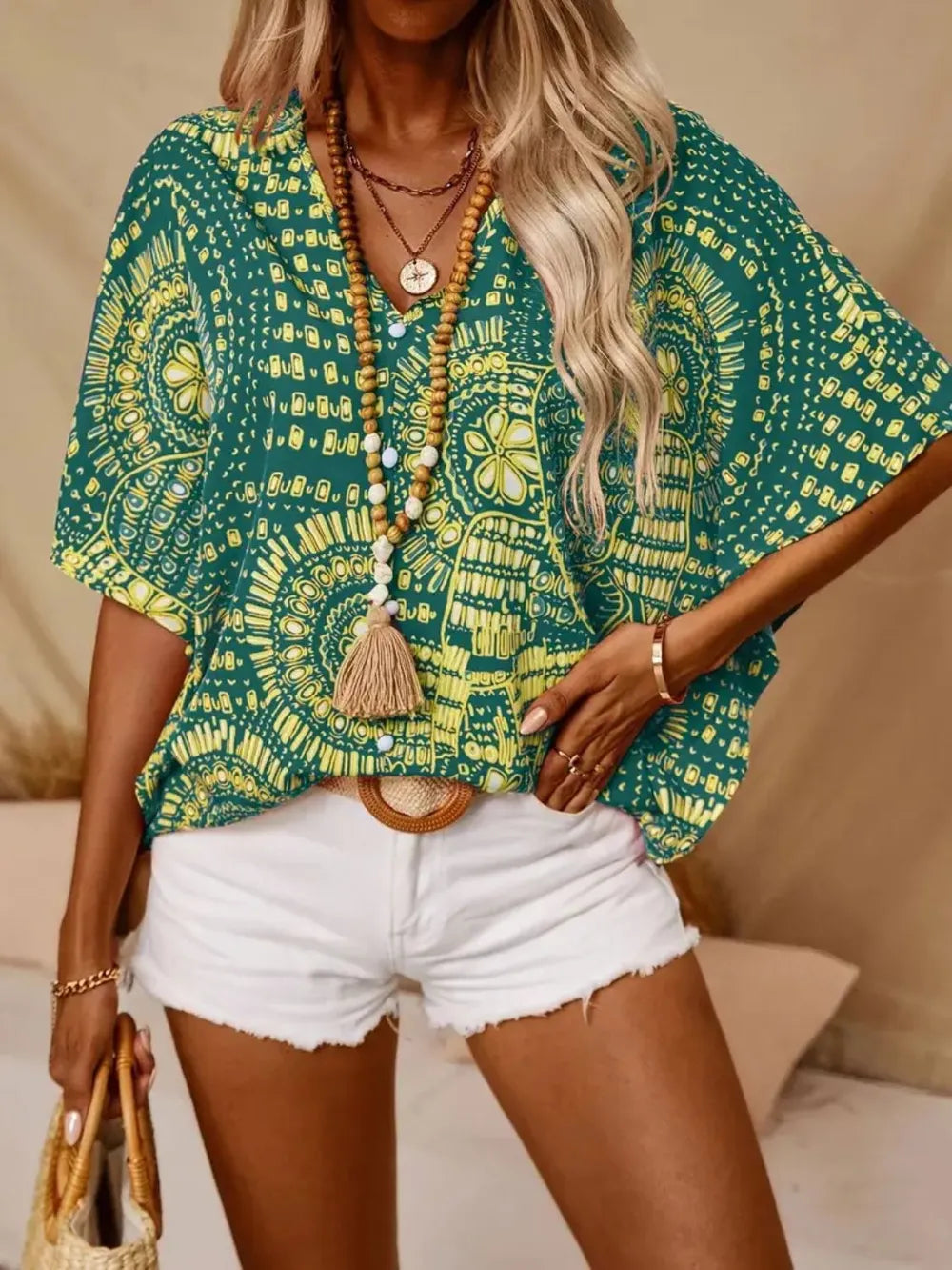 Green and yellow medallion-print blouse worn with white shorts and a woven handbag.