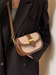 Cream patterned flap crossbody bag with brown trim and gold-coloured bar clasp, worn with a black coat