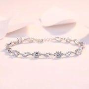 Silver-tone bracelet with repeating wavy links and small floral zircon clusters on a pink background