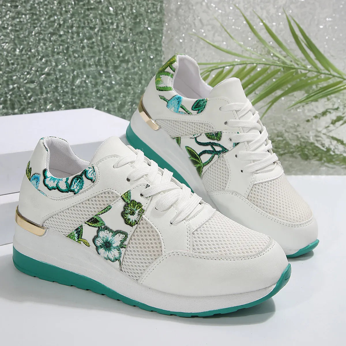 Pair of white sneakers with green floral panels and turquoise soles, side view