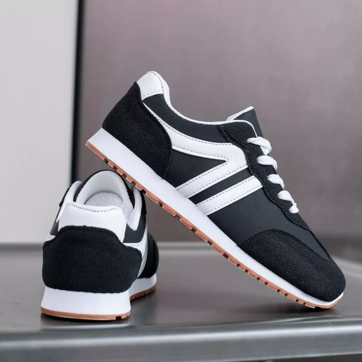 Black sneaker lifted to show its striped side, white sole and gum tread