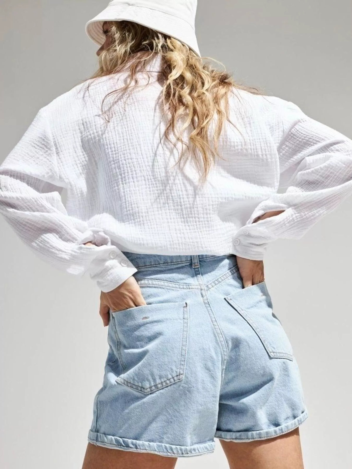 Model in white shirt and denim shorts with a bucket hat.
