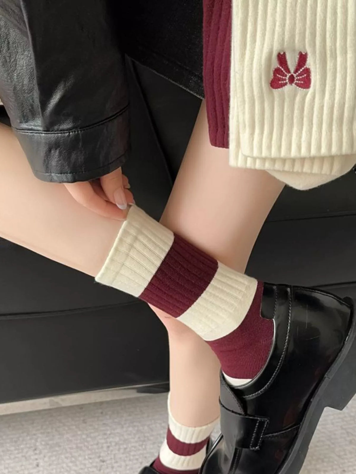 Cream ribbed sock cuff with a small burgundy bow motif, shown worn