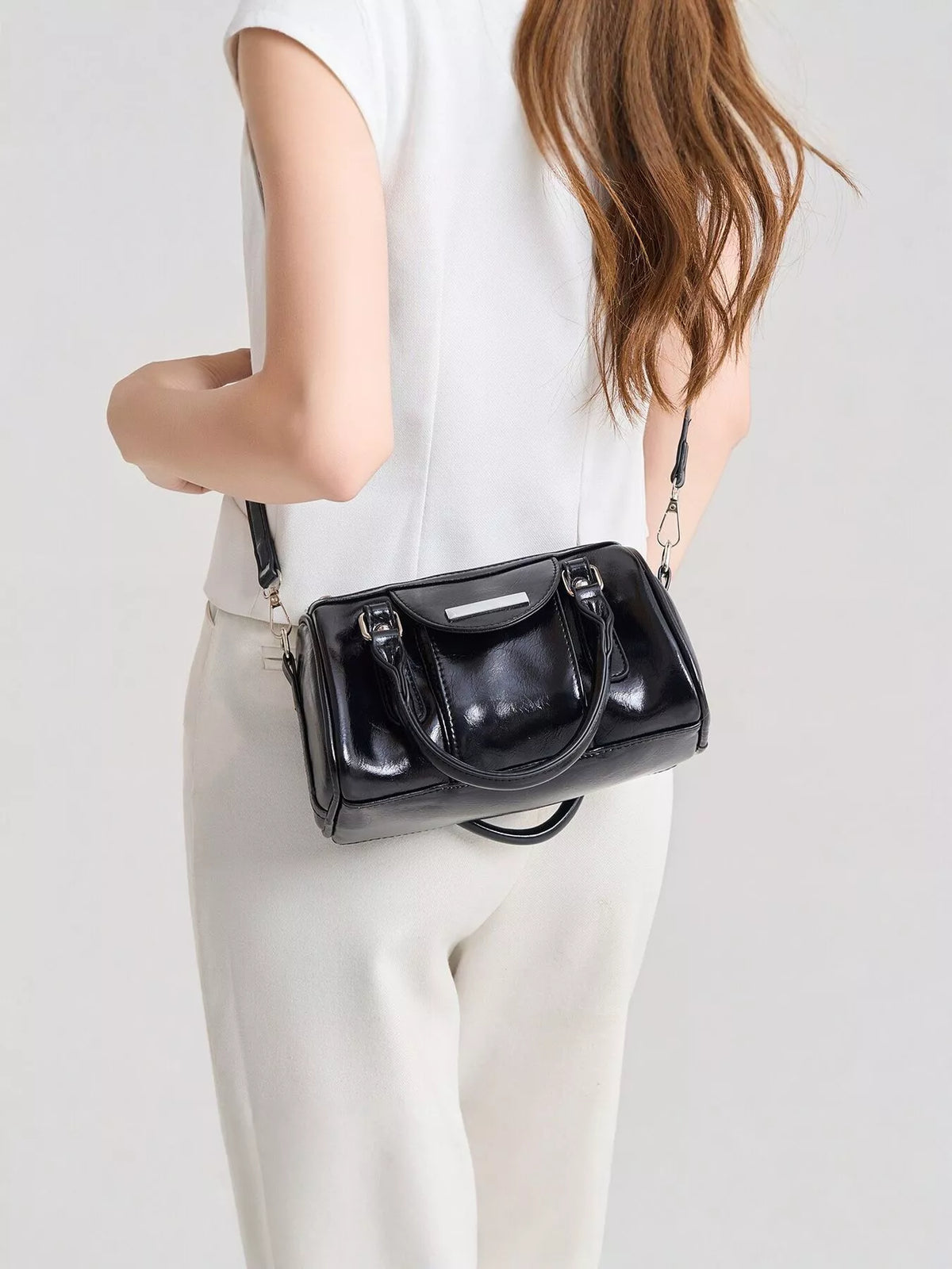 Black patent-look mini Boston bag worn crossbody at the hip, with short handles and front strap details.