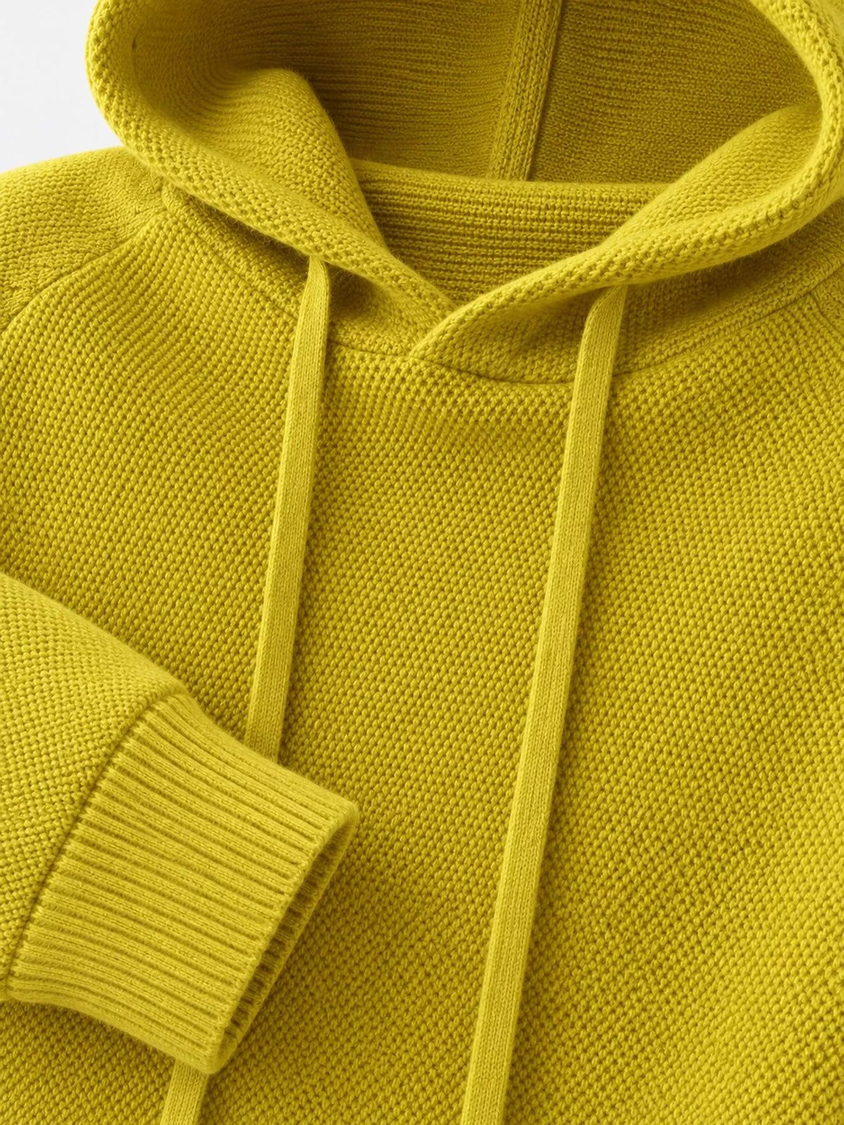 Mustard-yellow sweater close-up showing its hood opening, drawstrings and ribbed cuff.
