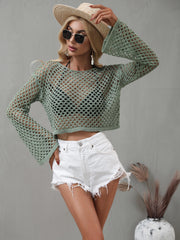 Model wearing a sage green open-knit cropped cover-up and posing with one hand on her hat.