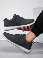 Grey knit lace-up shoe held beside a matching shoe worn on a foot