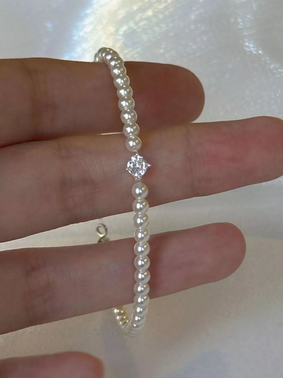 Close detail of the pearl strand and small silver-tone clasp held between fingers.
