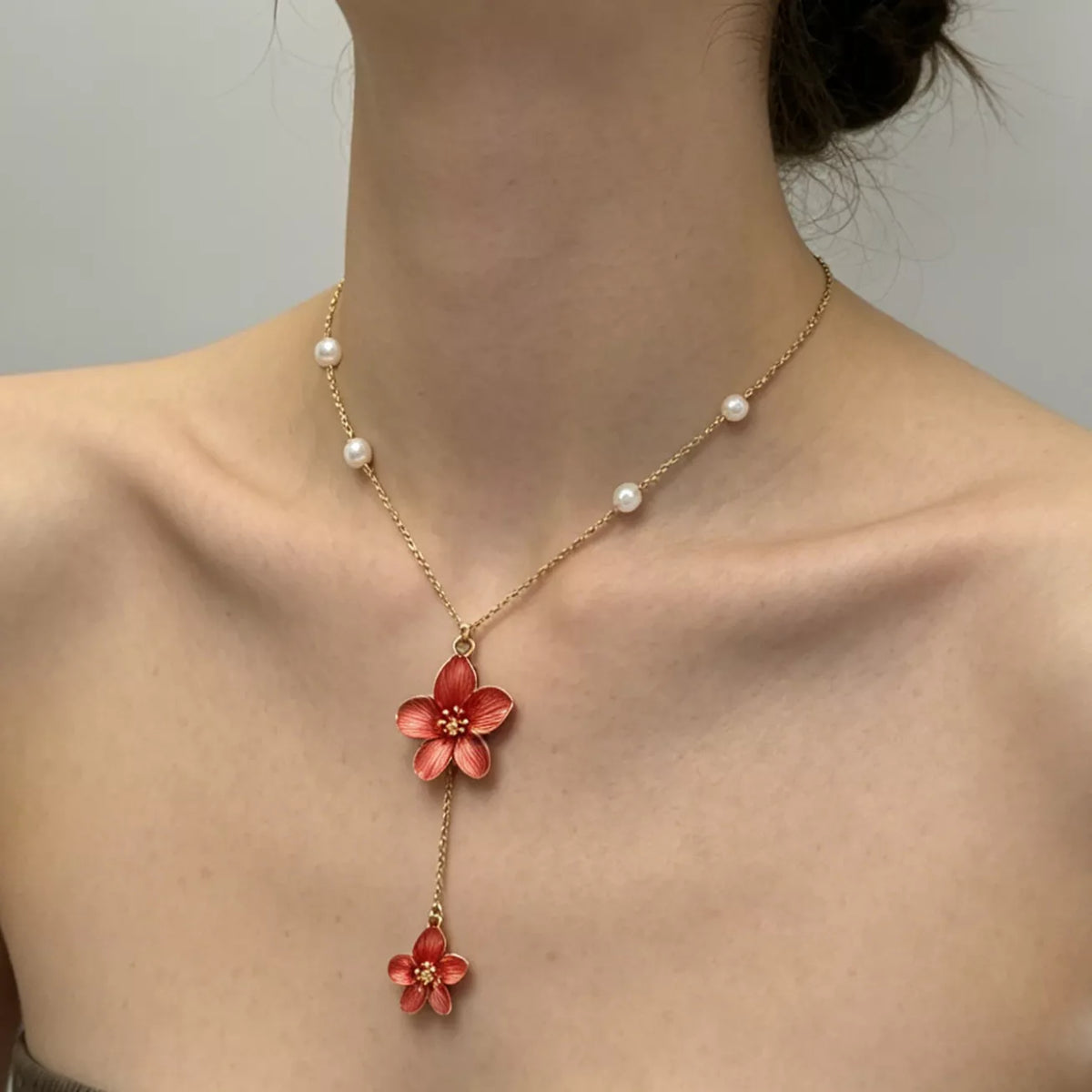 Gold-tone necklace with red flower drops shown from a side angle