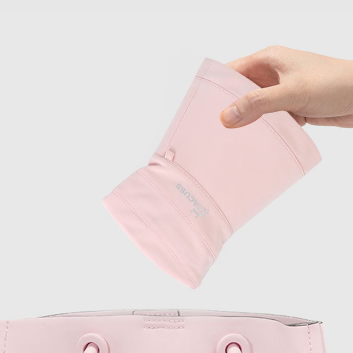 A hand folds the blush pink sun hat to show its flexible brim.