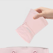 A hand folds the blush pink sun hat to show its flexible brim.